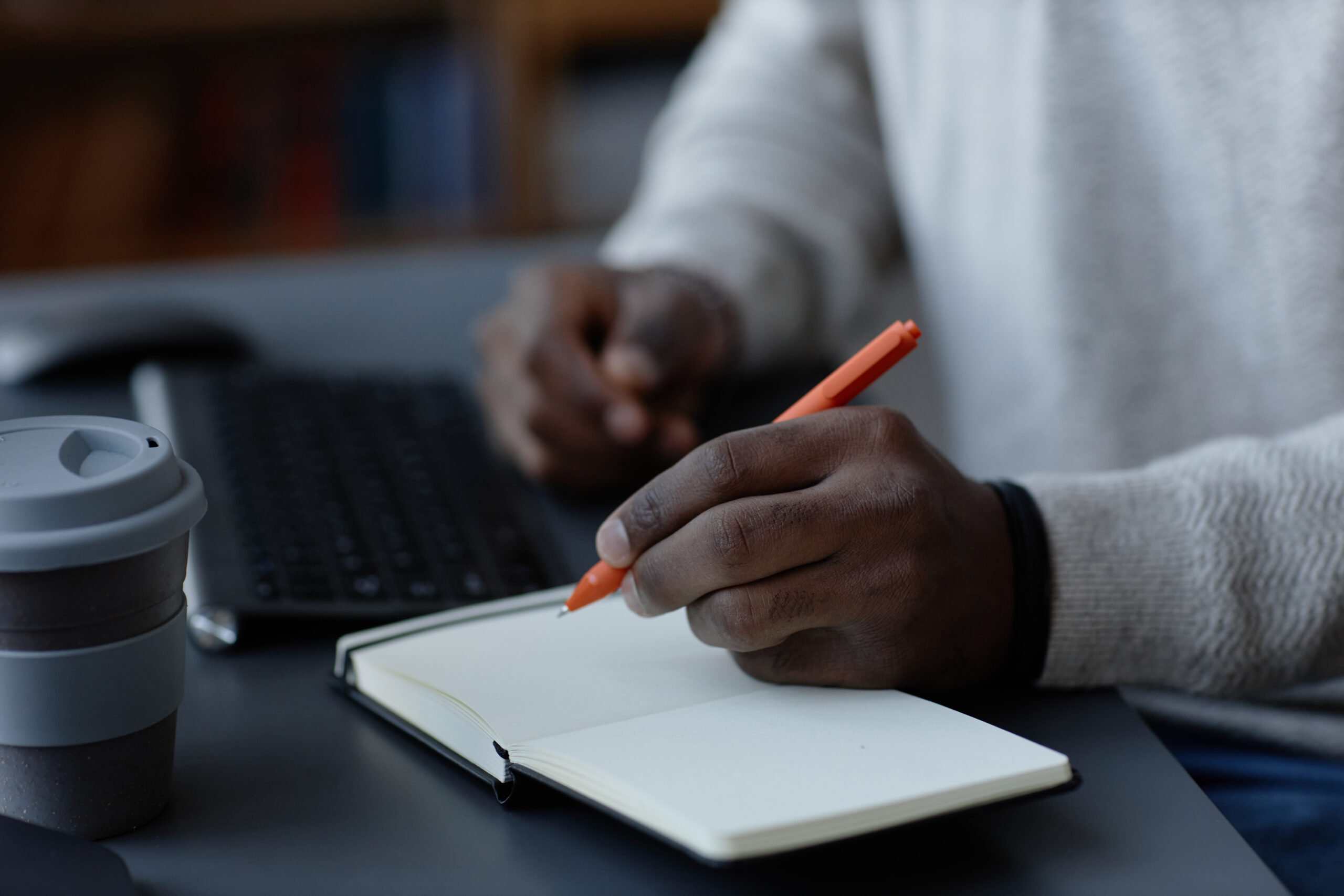 Black Man Writing in Notebook with Pen while Planning Work in Office